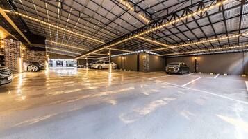 A spacious indoor parking garage with multiple cars parked, a high ceiling with exposed beams, and string lights.