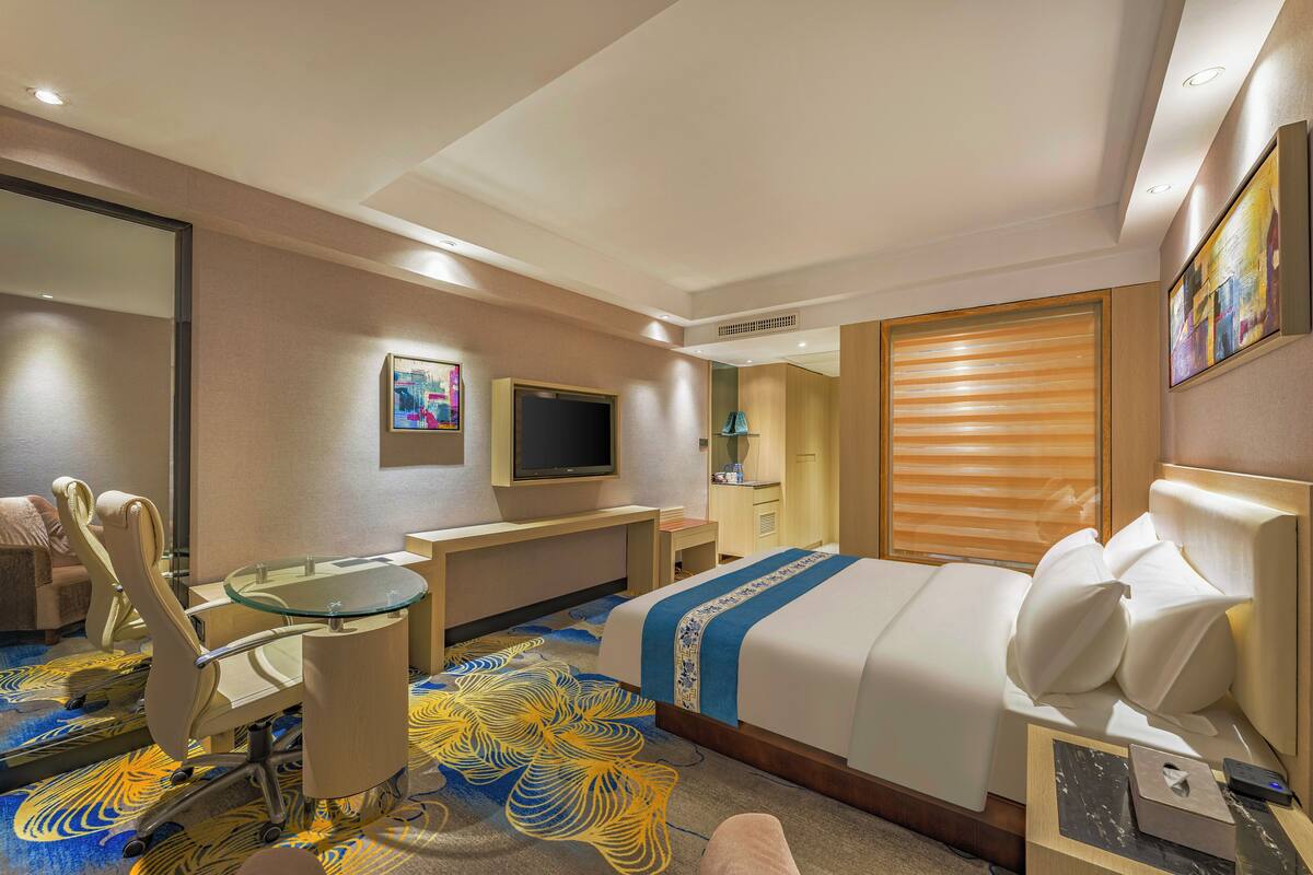 A hotel room with a bed, a desk, a chair, a TV, and a bathroom.