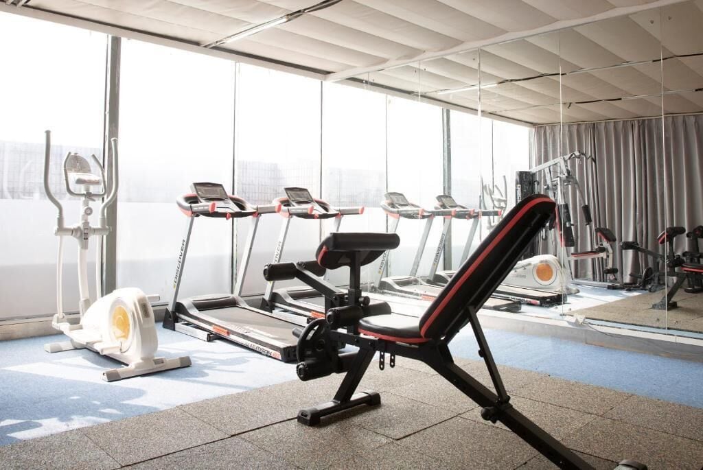 A gym with various exercise machines, large windows, and a ceiling with a grid pattern.