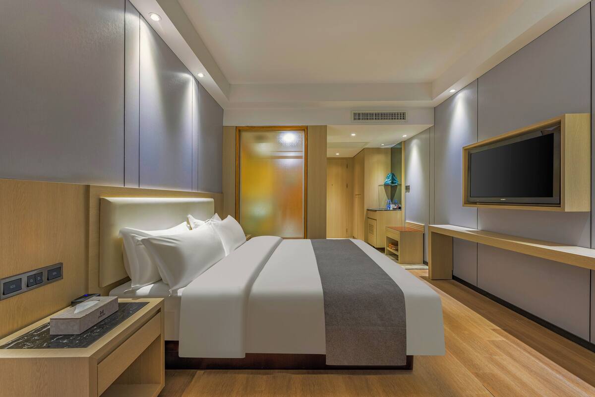 A modern hotel room with a large bed, bedside table, and a mounted TV.