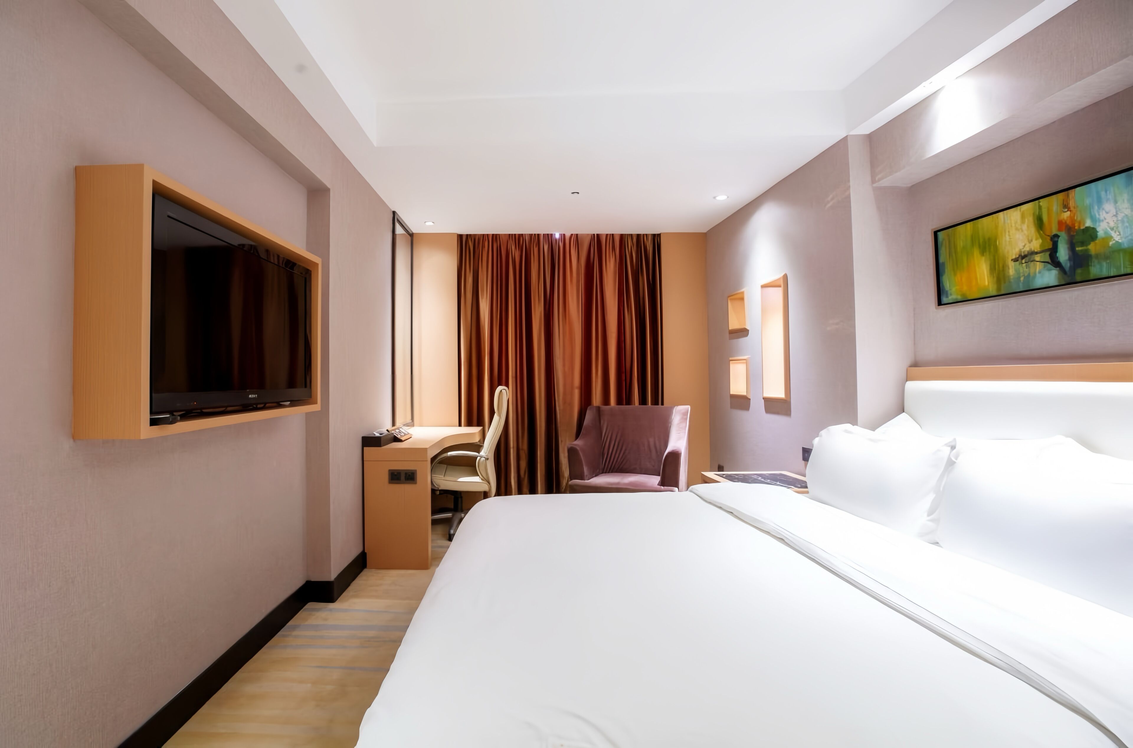 Habitación de hotel con una cama grande, un escritorio con silla, un televisor montado en la pared y un cuadro sobre la cama.