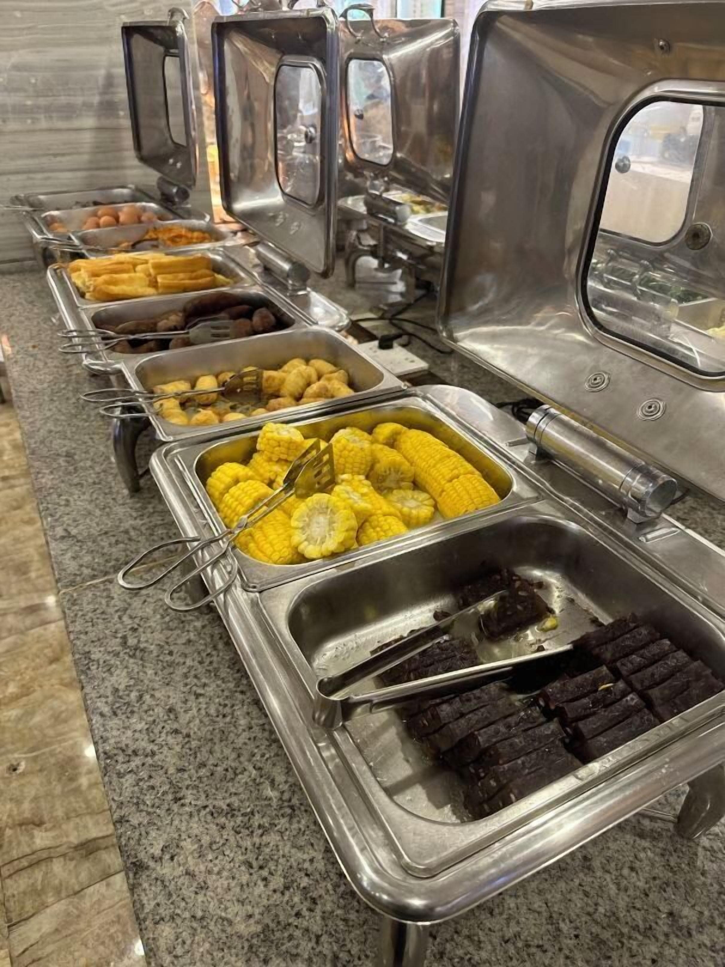 A buffet line with various food items including corn, meat, and other dishes.