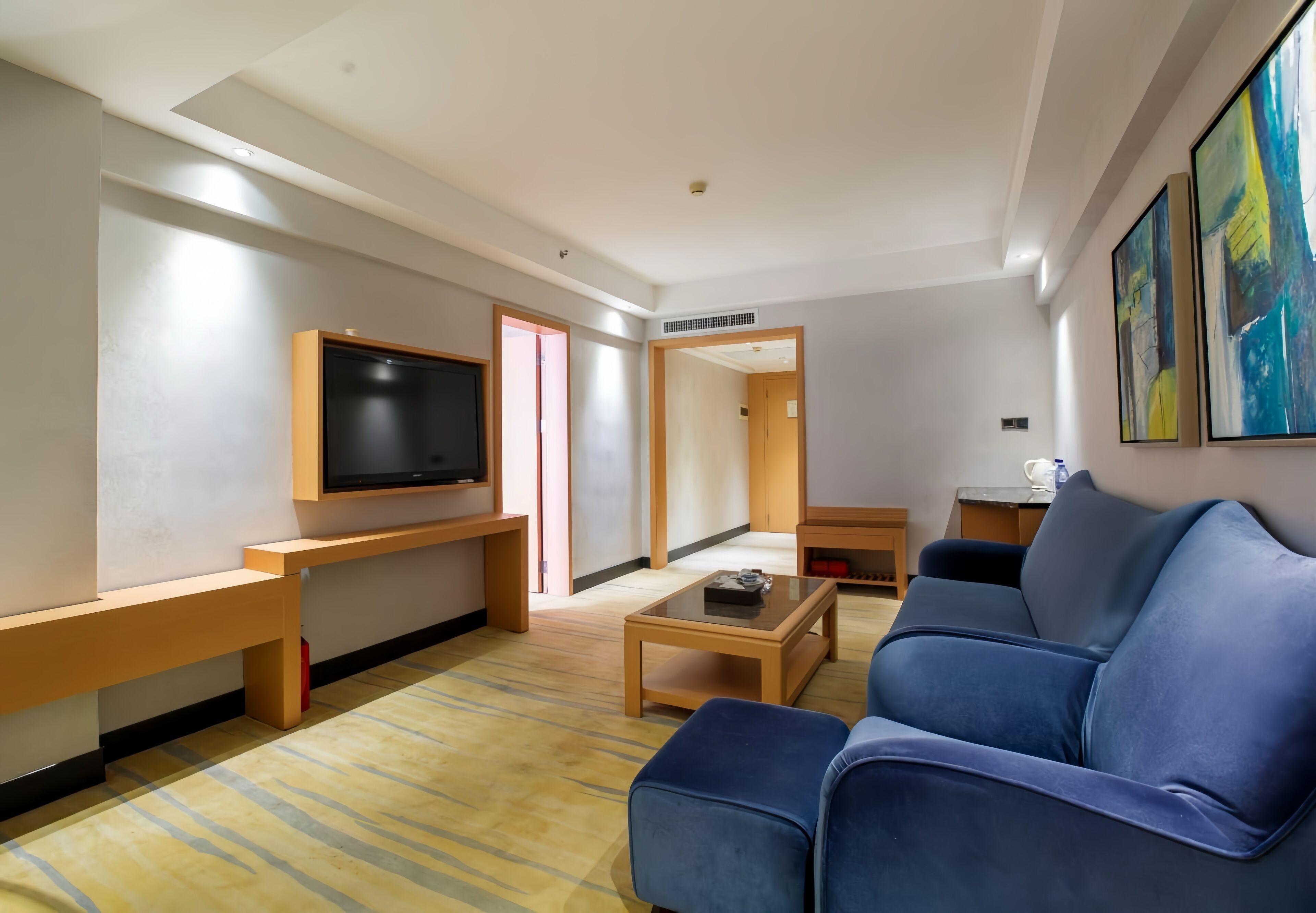 Een moderne woonkamer met een blauwe bank, een salontafel, een flatscreen televisie en een houten bankje.