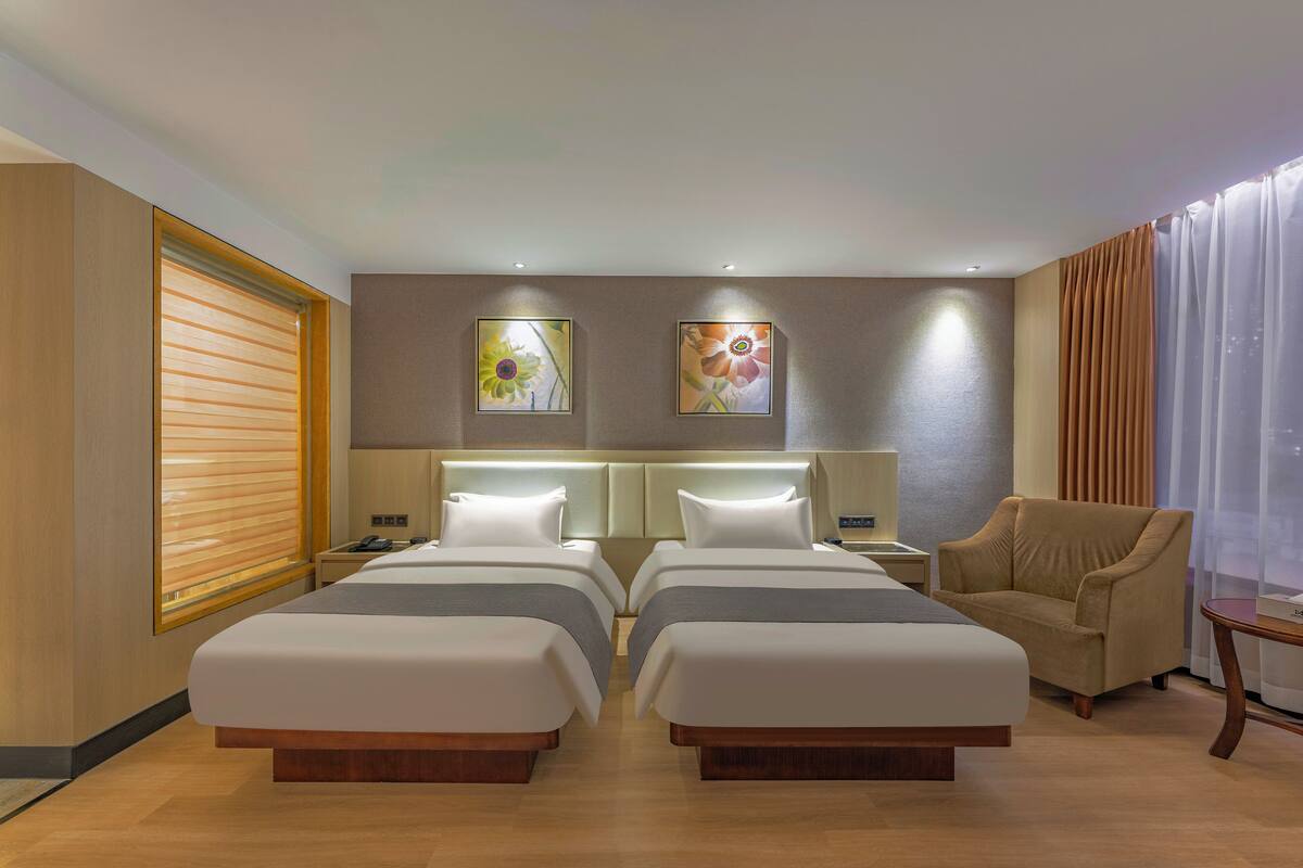 A hotel room with two beds, a sofa, a nightstand, and a window with curtains.