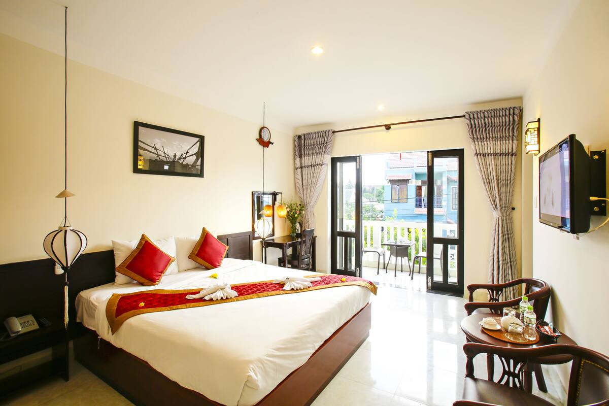 A hotel room with a large bed, a desk with a chair, a TV, and a balcony with a view.