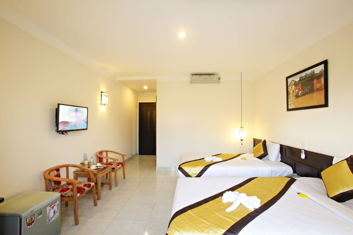 A hotel room with two beds, a TV, a desk with chairs, and a refrigerator.