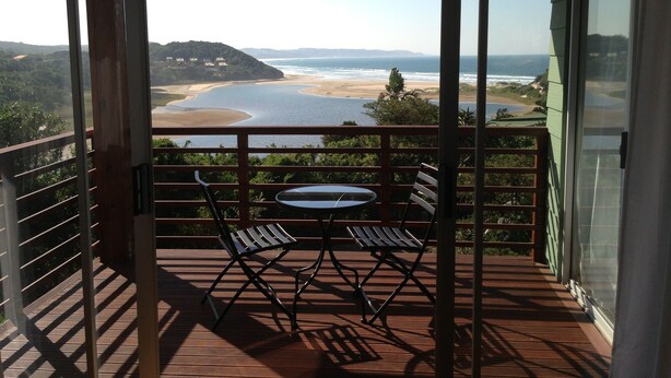 A balcony with a table and chairs, overlooking a beach and ocean. - Buccaneers Backpackers (Great Kei)