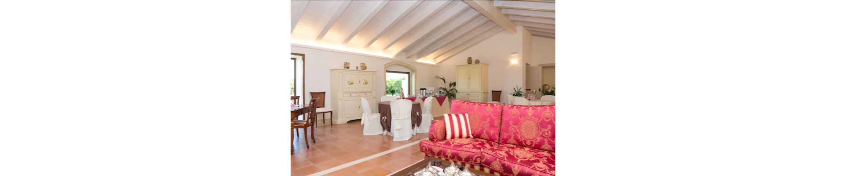 A spacious living area with a high ceiling, a dining table set with chairs, and a sofa with patterned upholstery.