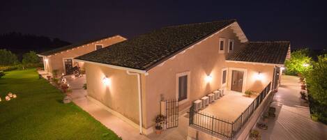 Una casa de dos pisos con un porche cubierto, plantas en macetas e iluminación exterior.