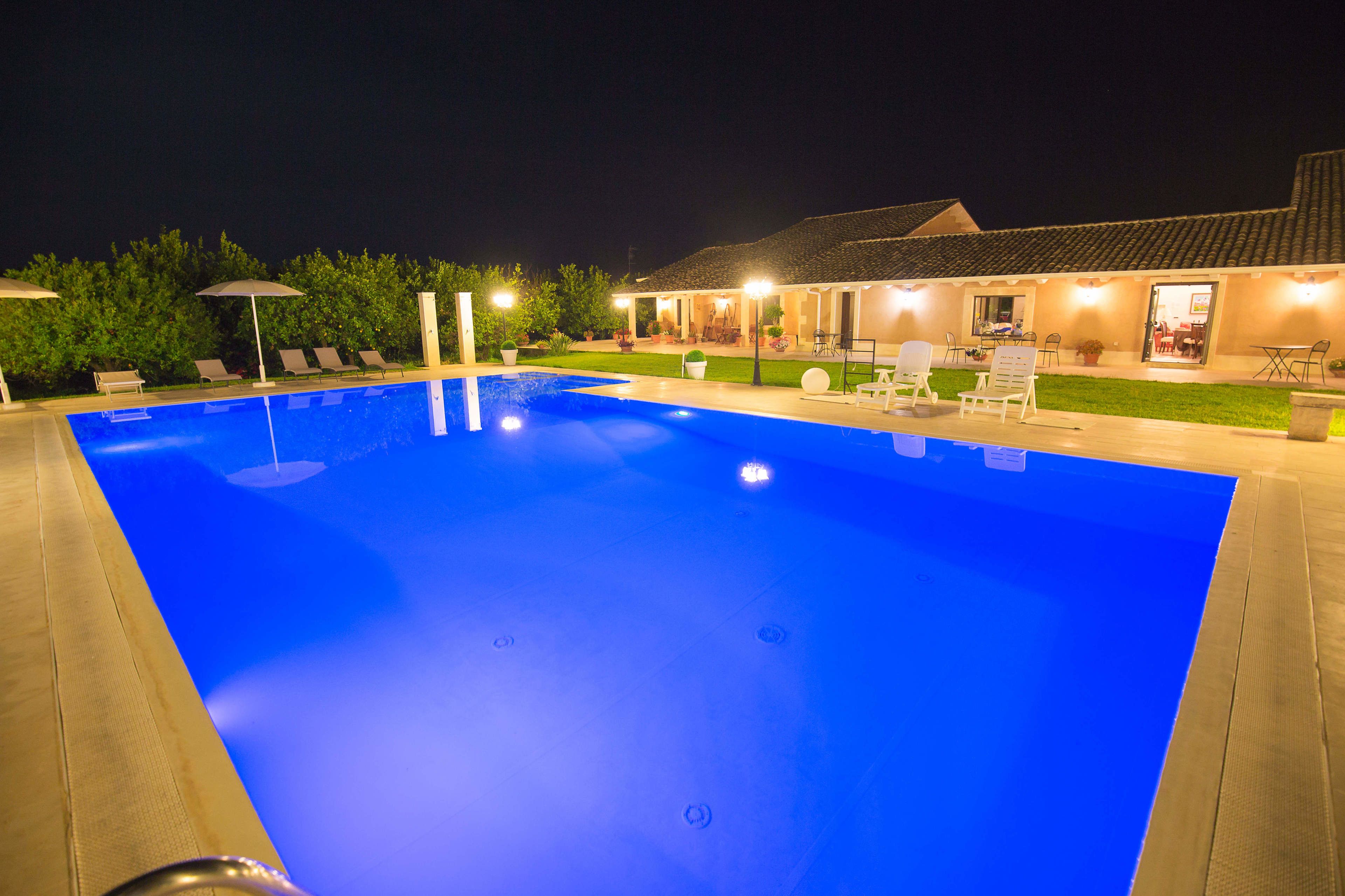 A swimming pool with lounge chairs and umbrellas, surrounded by a well-lit patio area.