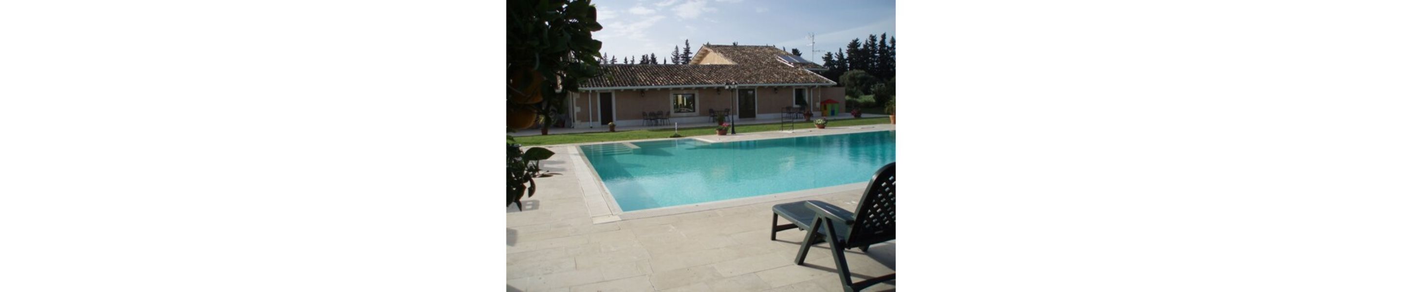 Une piscine avec une terrasse carrelée, un fauteuil de relaxation et, au fond, un bâtiment dont le toit est également recouvert de carreaux.