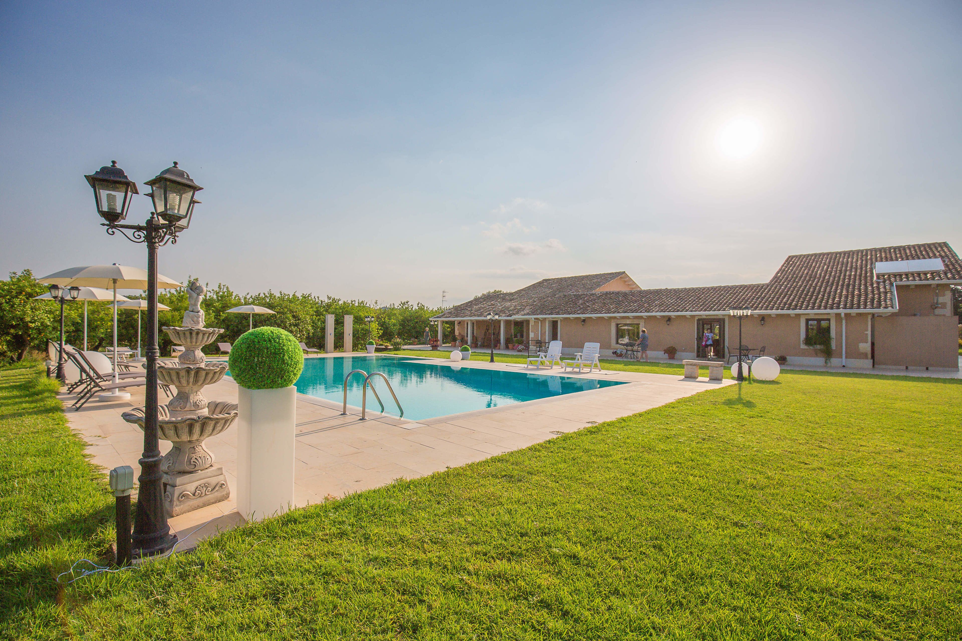 Une piscine avec des chaises longues, une statue et un lampadaire.