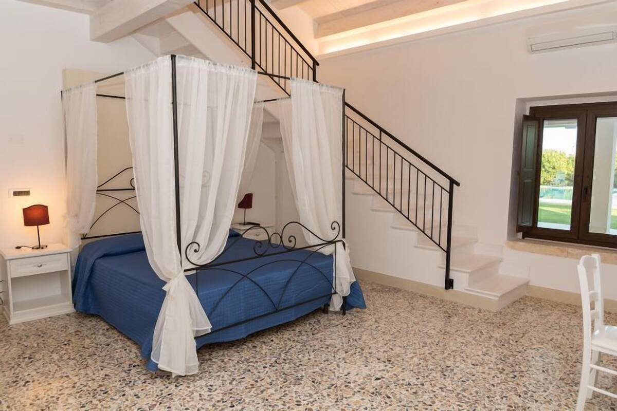 Ein Schlafzimmer mit einem Himmelbett, einem Nachttisch mit Lampe, einem Fenster mit Blick und einer Treppe.