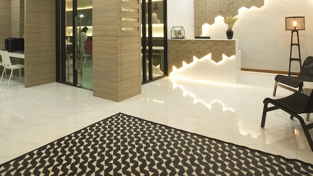 Uma área de recepção moderna com uma luminária geométrica, balcão de recepção e tapete estampado.