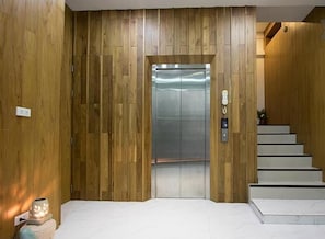 Un elevador revestido de madera con un diseño moderno, escalones blancos que conducen hacia él y una pequeña mesa con una luz en el lado izquierdo.