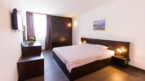 A bedroom with a bed, bedside table, lamp, wardrobe, and a painting on the wall. - Hotel Omorika (Punat)
