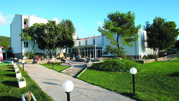 A modern building with a paved walkway, outdoor seating area, and well-maintained greenery. - Hotel Omorika (Punat)