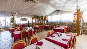 A restaurant with multiple tables and chairs, a stone wall, and a ceiling fan. - Hotel Omorika (Punat)