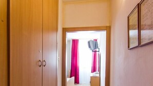A narrow hallway with a red carpet leading to a room with a bed, a television, and a small table. - Hotel Omorika (Punat)