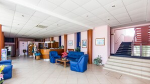 A hotel lobby with a reception desk, blue sofas, a coffee table with flowers, and a staircase. - Hotel Omorika (Punat)