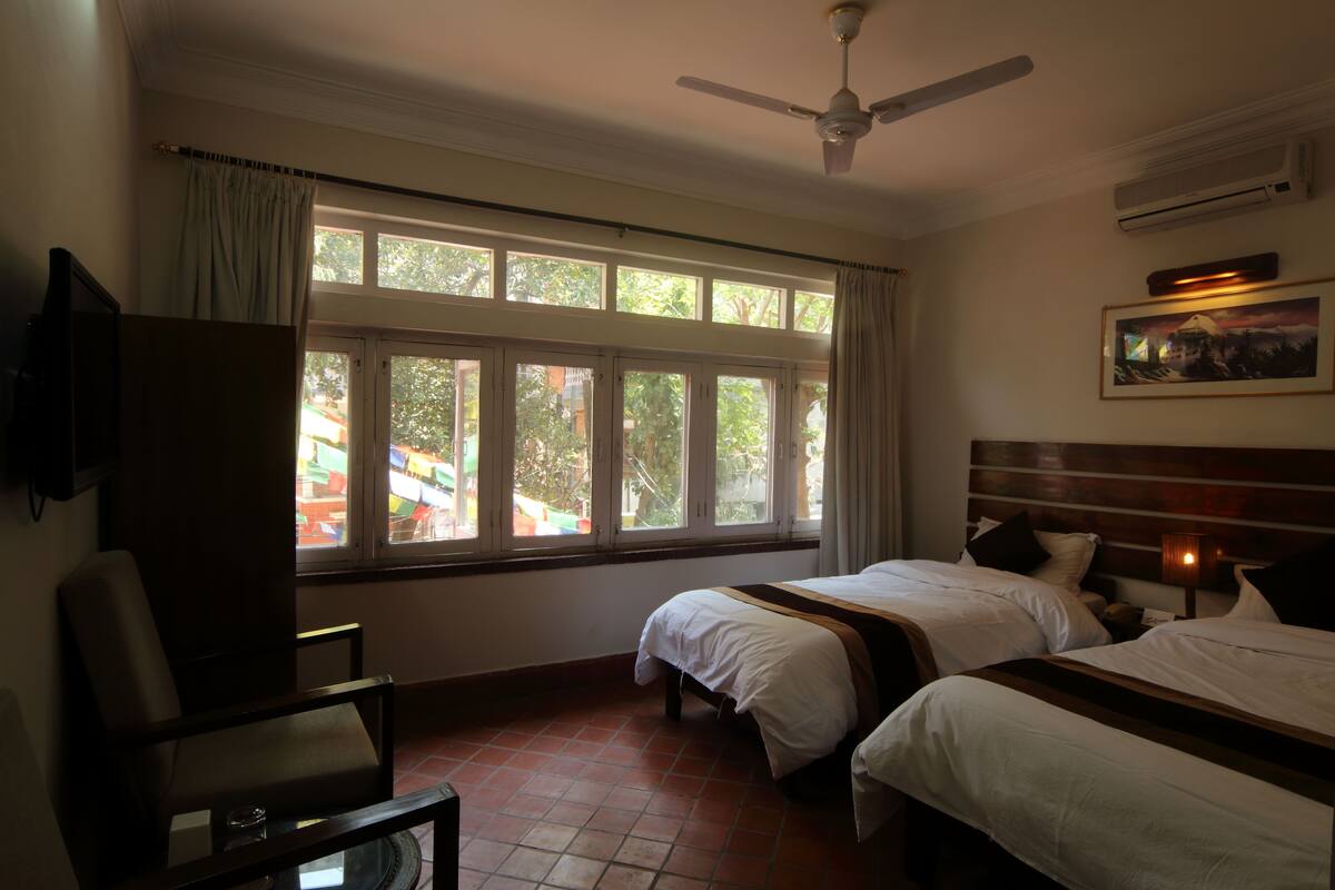 A hotel room with two beds, a ceiling fan, a TV, and a window with curtains.