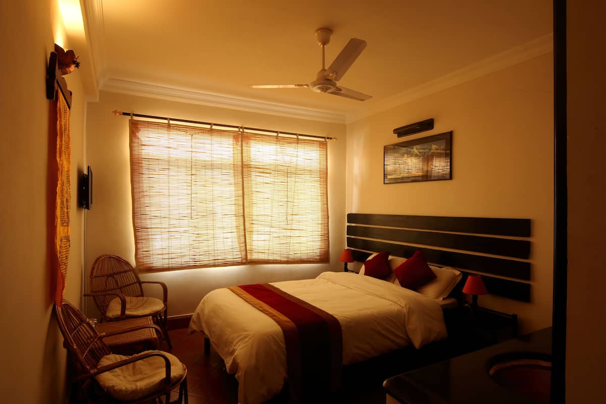 A bedroom with a bed, two chairs, a nightstand, a ceiling fan, and a window with blinds.