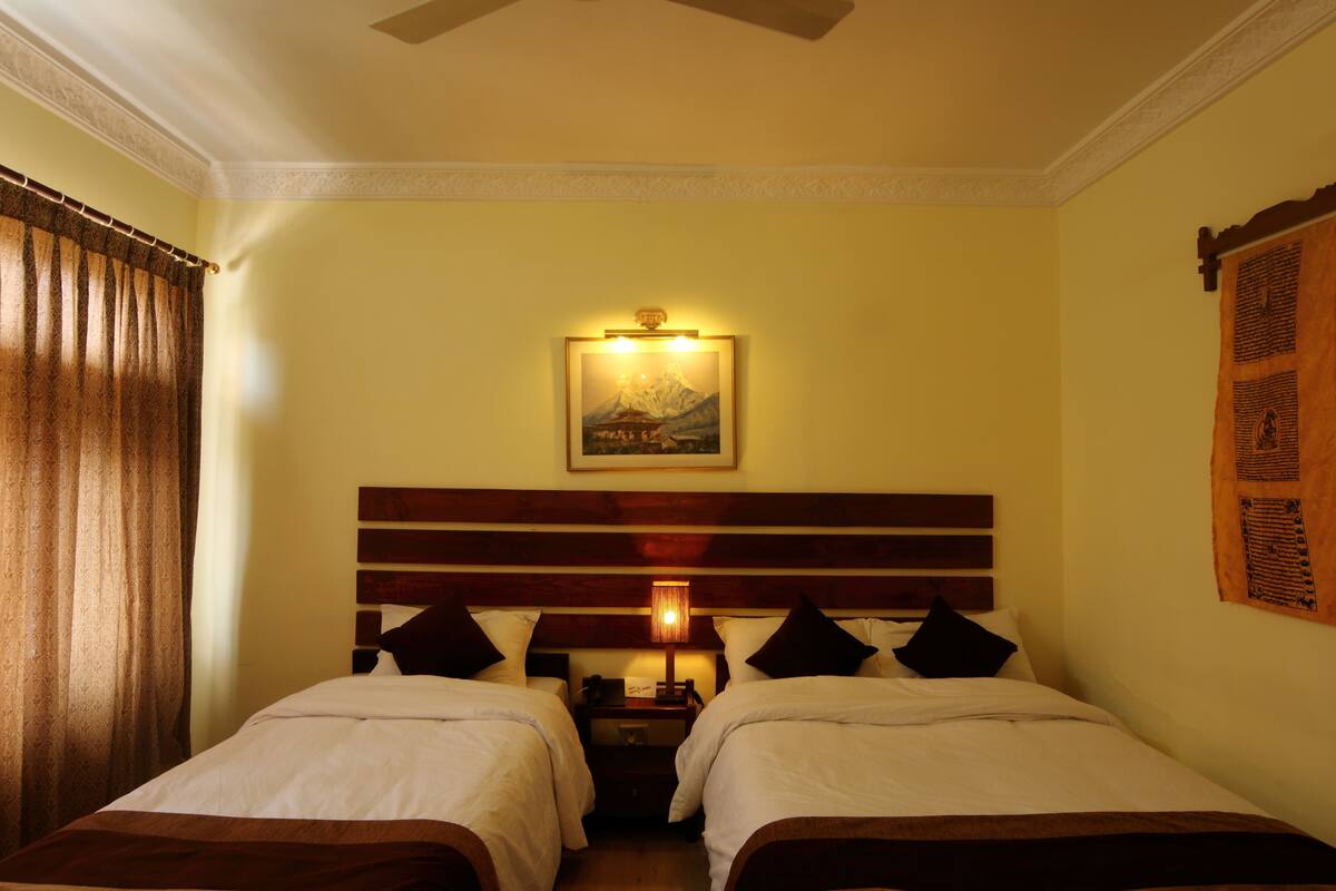 A hotel room with two beds, a nightstand, a lamp, a framed picture on the wall, and a curtain.