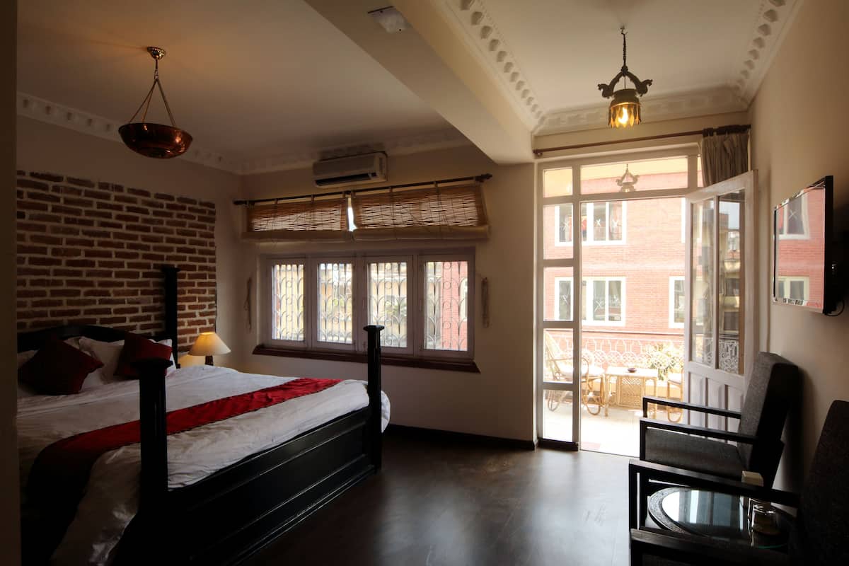A bedroom with a brick wall, a bed with a red and white bedspread, a window with a view of the outside, and a chair by the window.