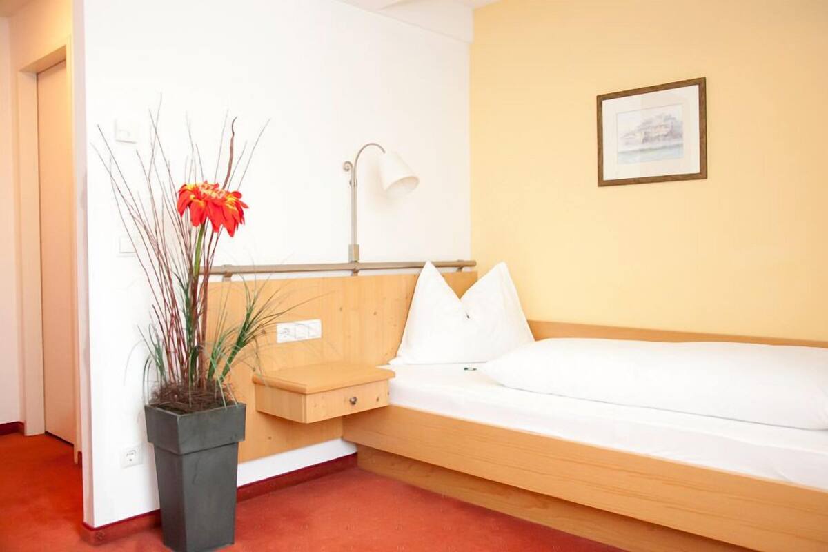 Un dormitorio pequeño con una cama individual, una mesita de noche, una lámpara y un cuadro enmarcado en la pared.