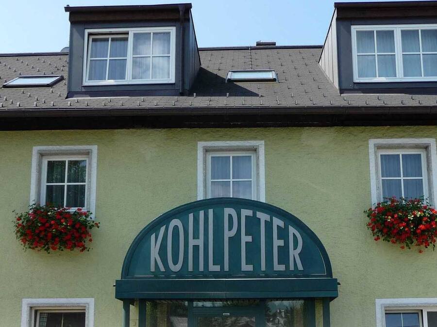 Un edifici amb façana verda, diverses finestres i un rètol que diu "KOHLPETER".