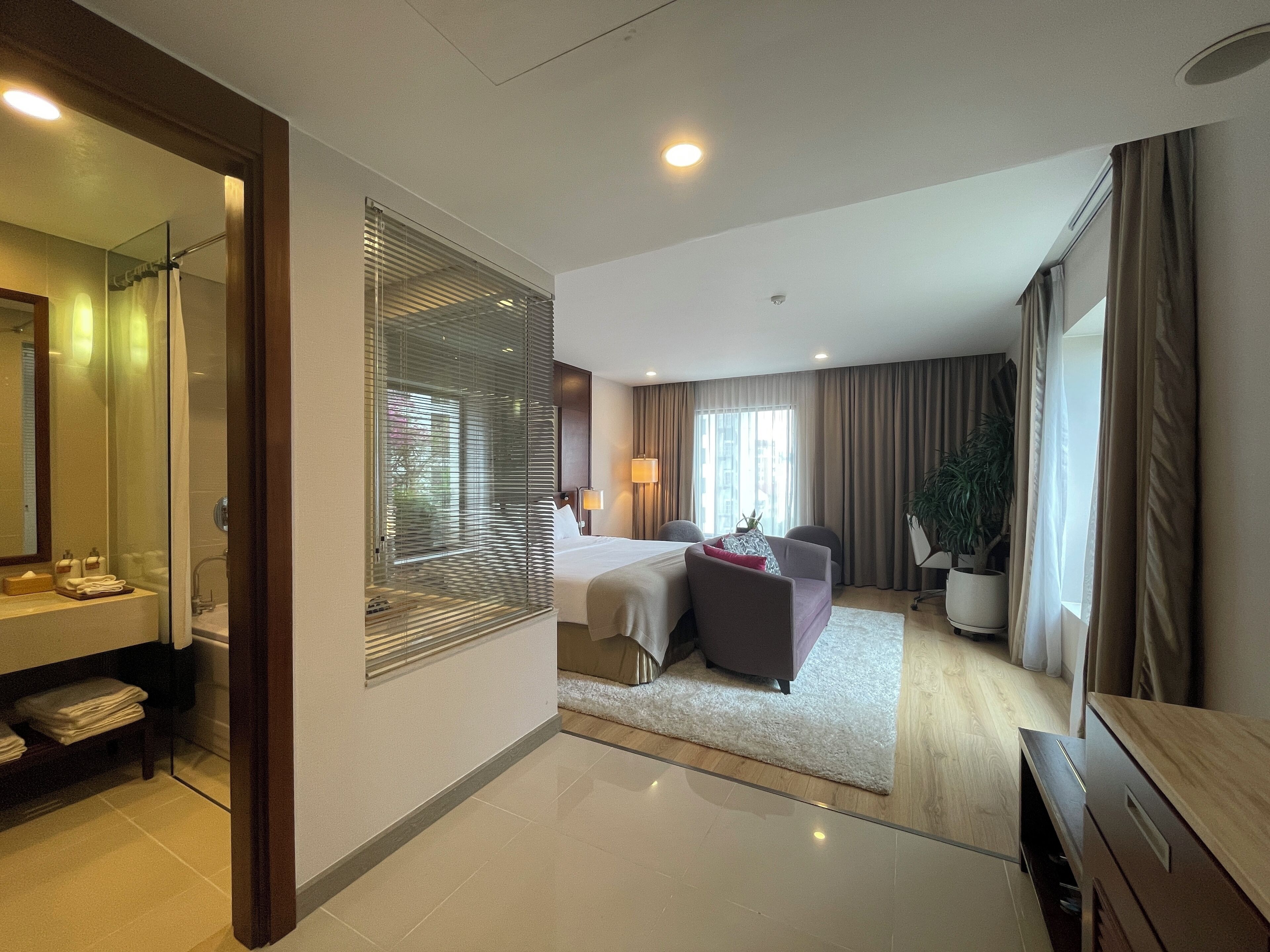Een moderne hotelkamer met een groot bed, een zithoek, een badkamer met een douchecabine van glas en uitzicht op de stad.