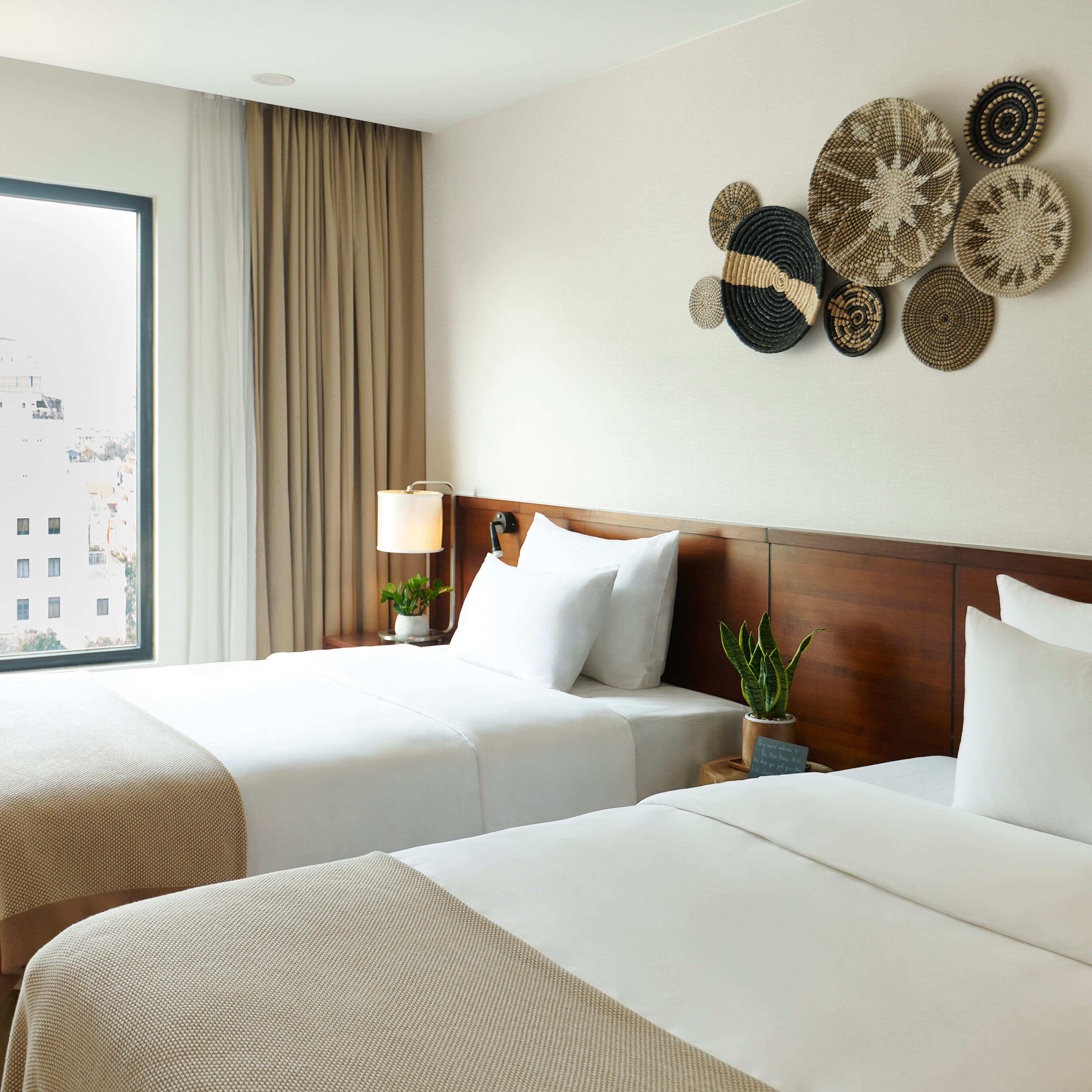A hotel room with two beds, a large window, a lamp, and decorative wall art.