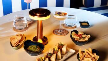 A round table with various dishes, a cocktail, and a small bowl of breadsticks.