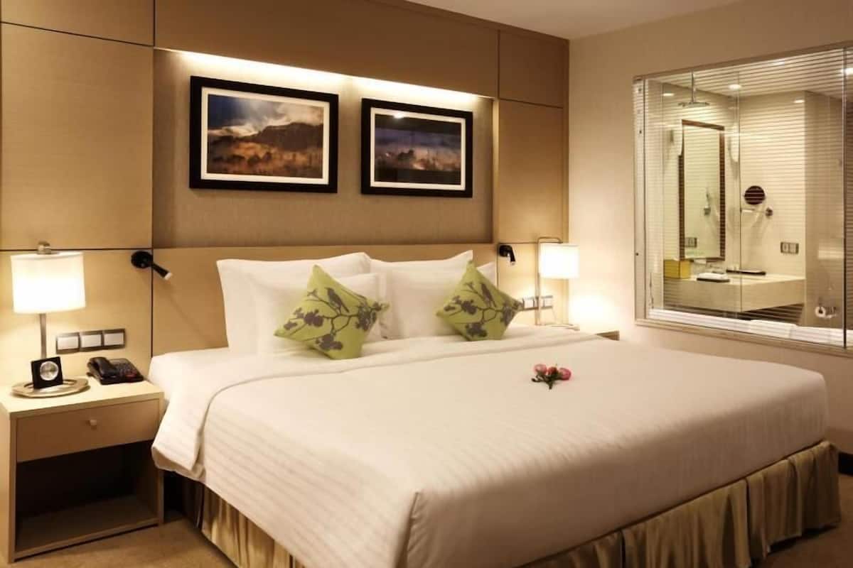 Quarto de hotel com uma cama grande, duas luminárias de cabeceira, uma mesa de apoio, um espelho e duas imagens emolduradas na parede.