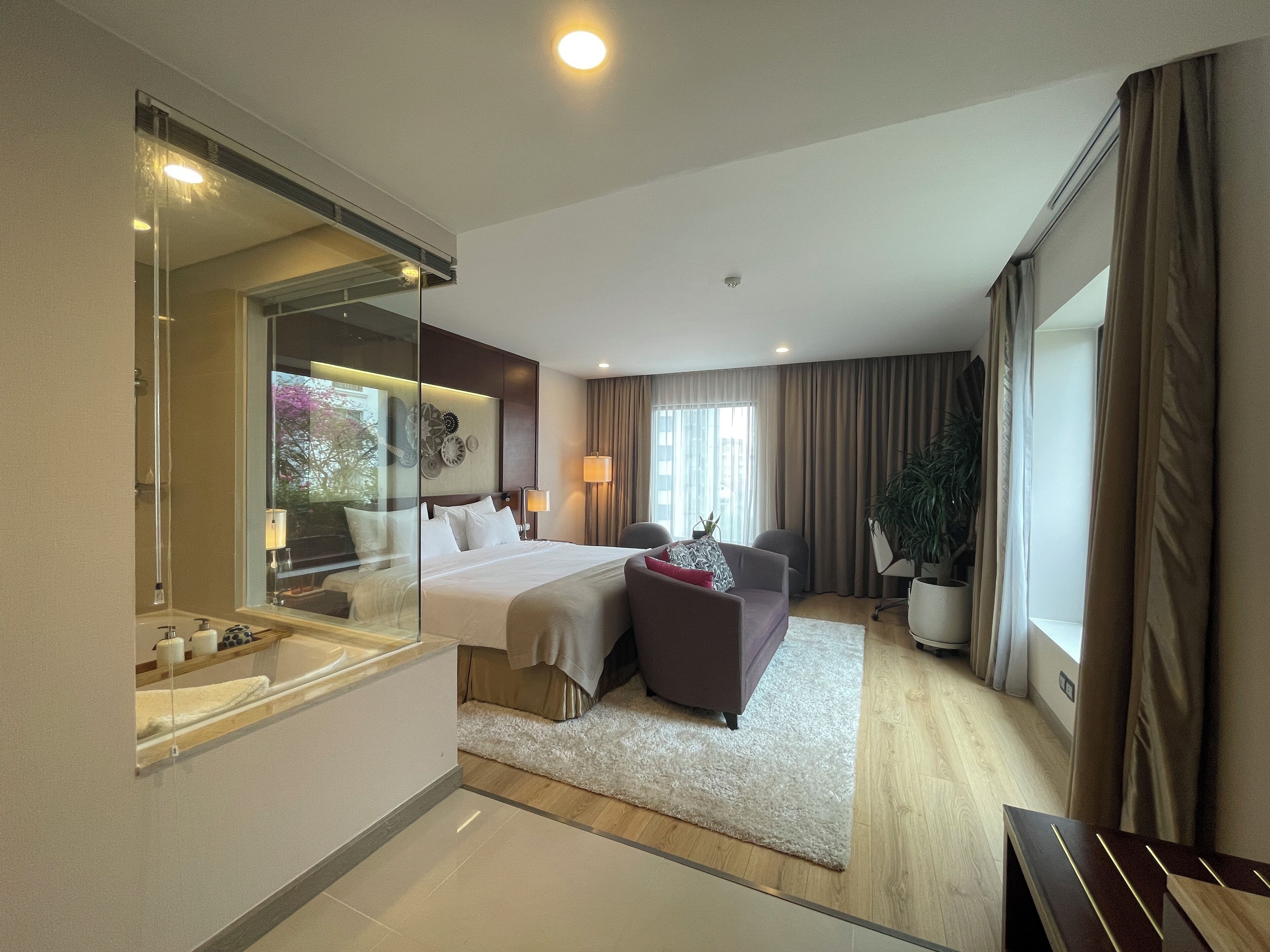 Une chambre d’hôtel moderne avec un grand lit, un coin salon, un grand miroir et une plante en pot.