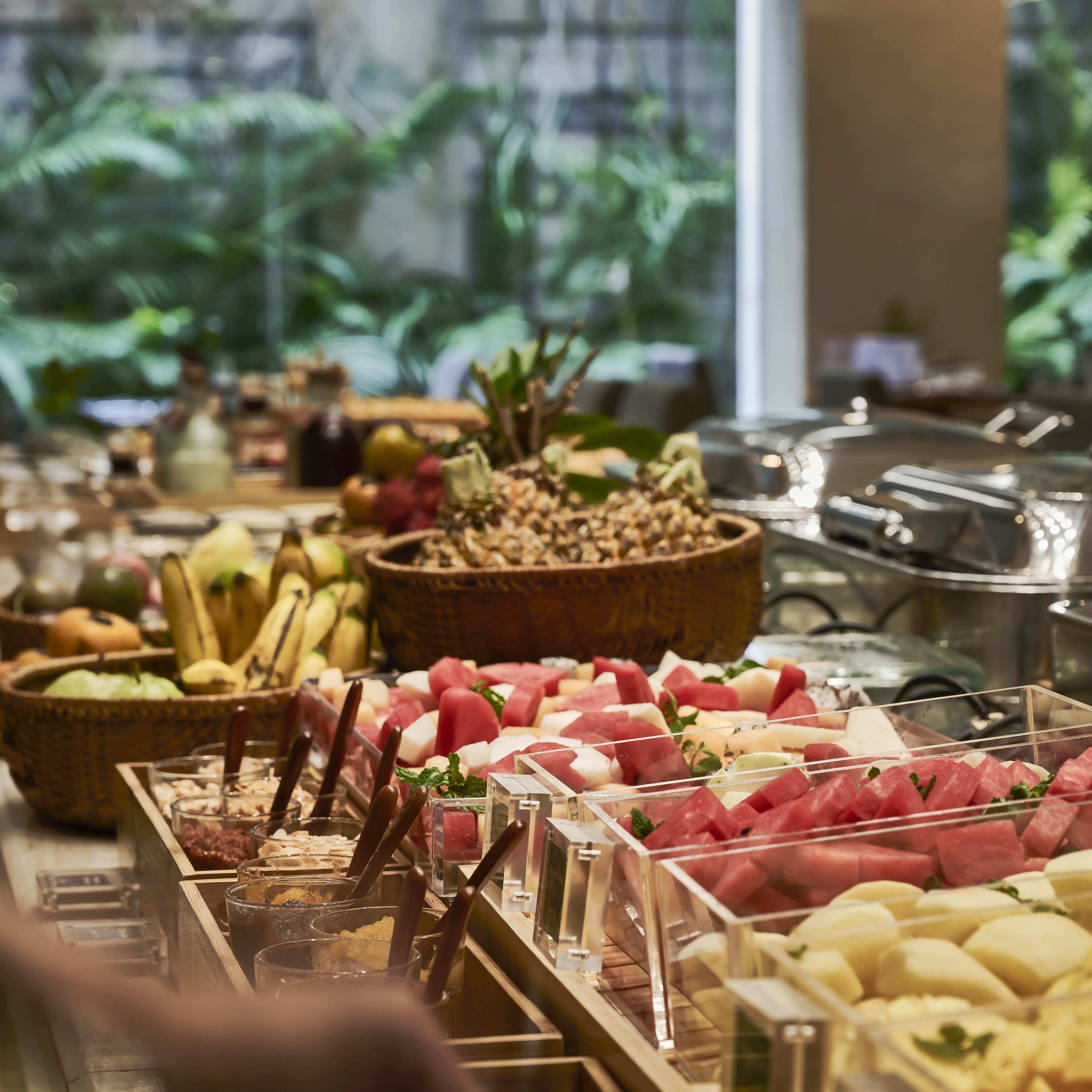 A buffet with various fruits and vegetables, including watermelon and bananas, arranged in wooden bowls and clear containers.