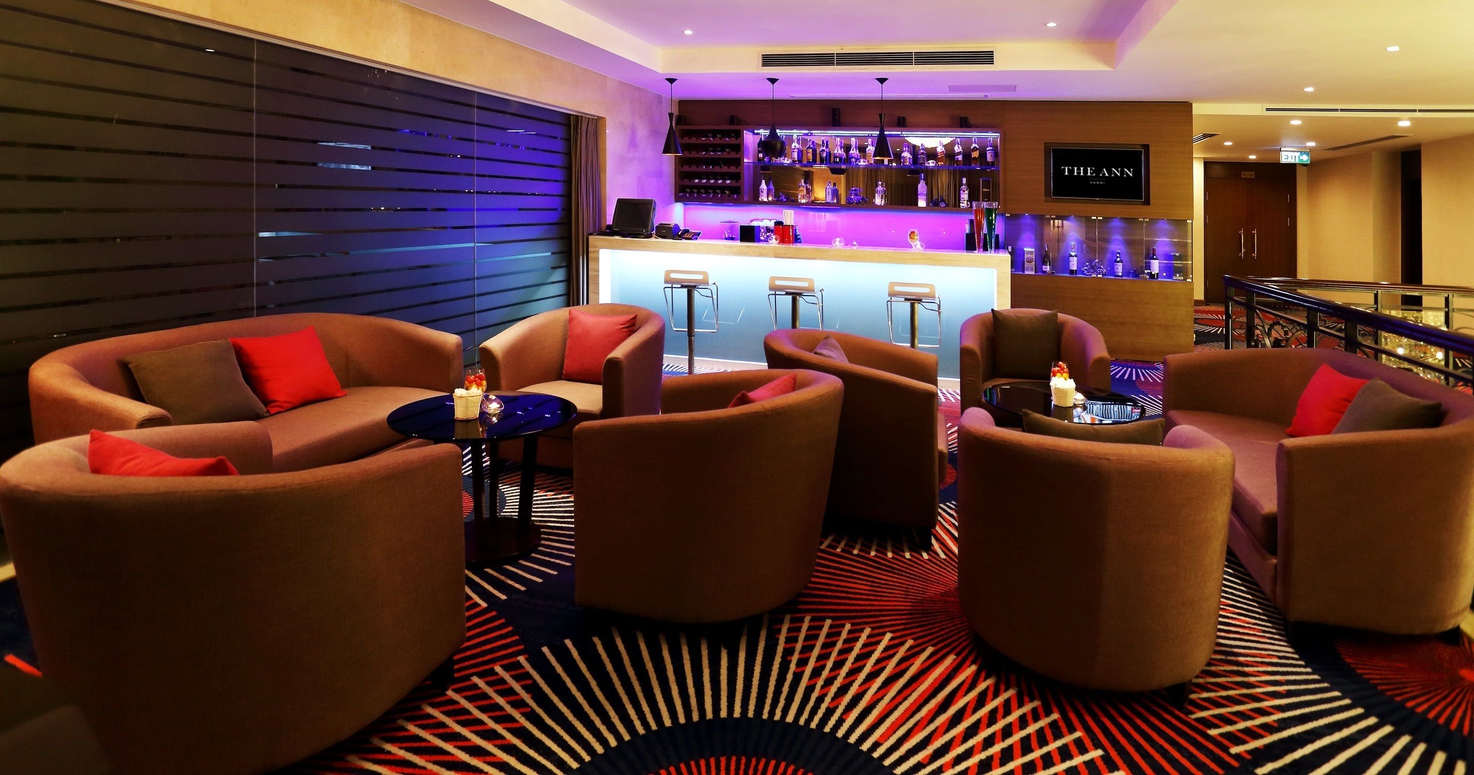 A modern bar area with a bar counter, multiple seating options including sofas and chairs, and a patterned carpet.