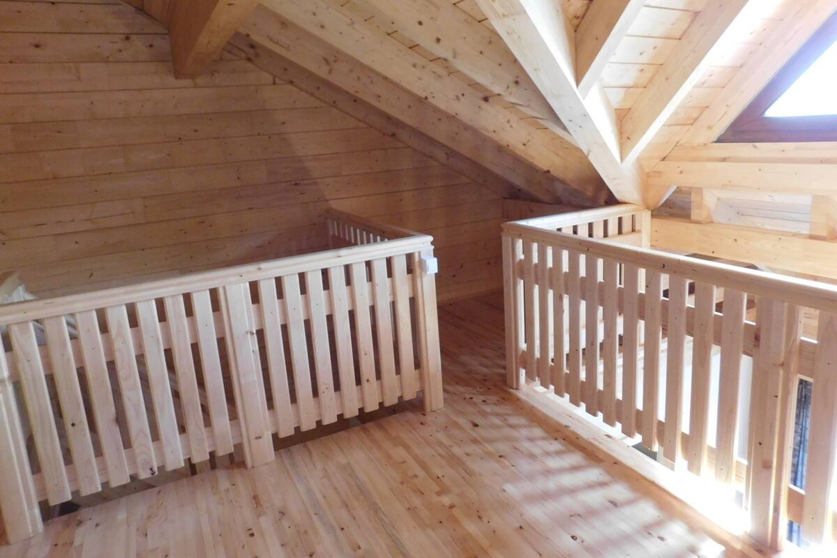 An attic room with wooden floors, a sloped ceiling, and a white railing.