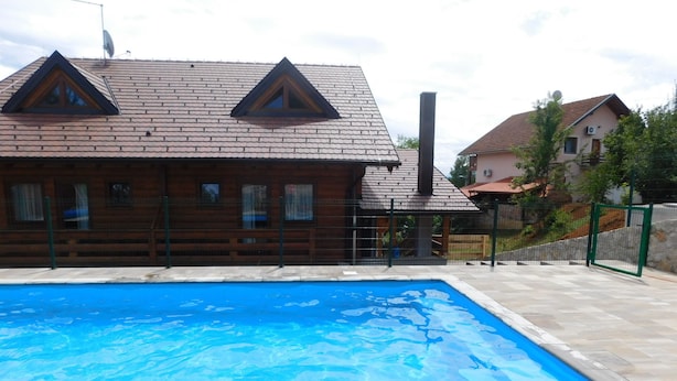 Ein Schwimmbad mit Holzterrasse, eine Holzhütte mit geneigtem Dach und eine Steinmauer im Hintergrund.