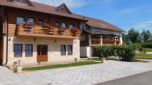 Ein zweistöckiges Holzhaus mit Steinmauern, Balkonen mit Blumenkästen und einer gepflasterten Auffahrt.
