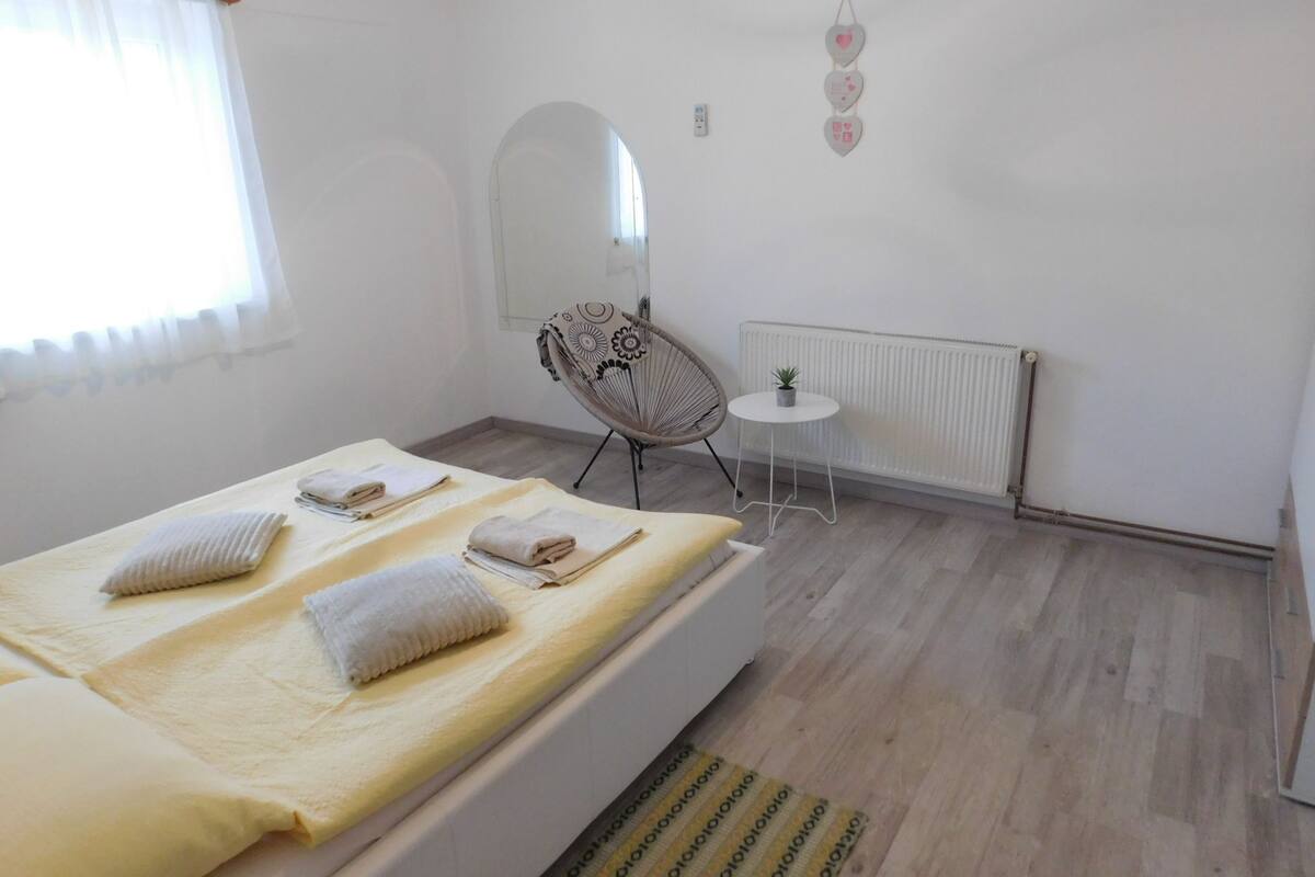 A bedroom with two beds, a chair, a small table, a radiator, and a mirror.