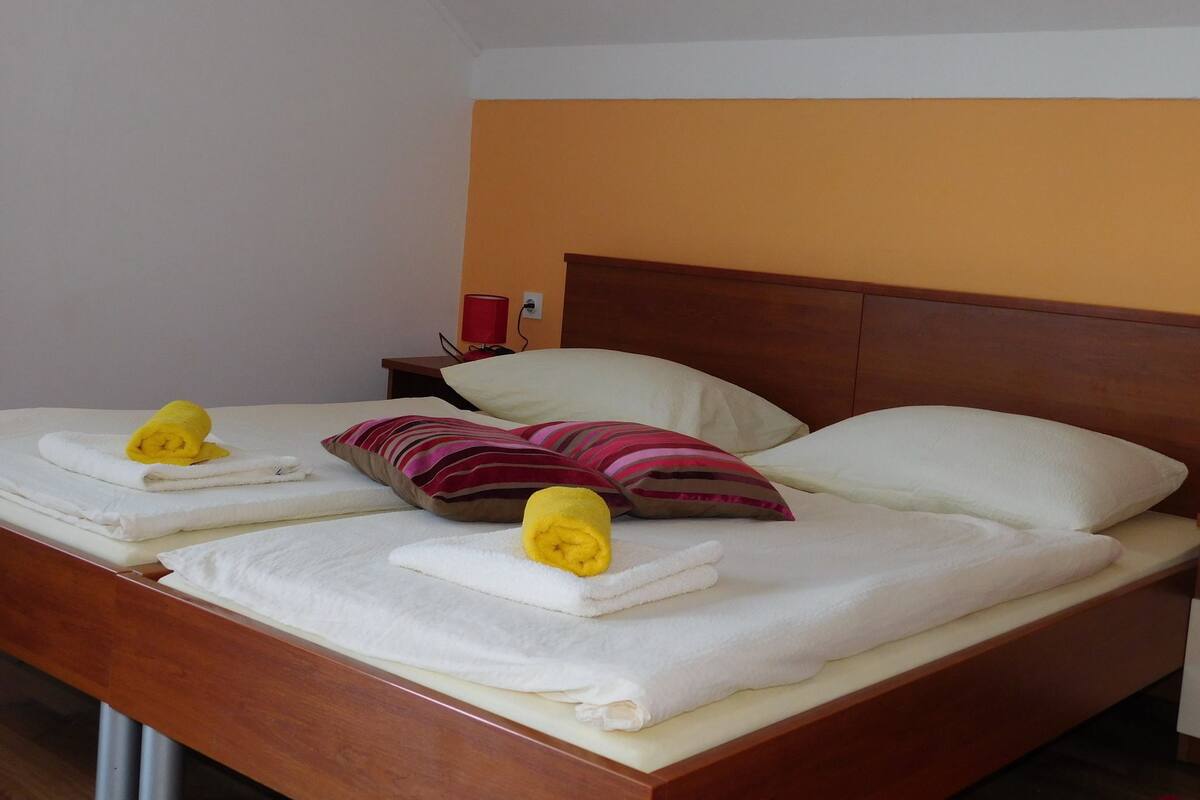 A neatly made bed with white linens and two yellow towels rolled at the foot.