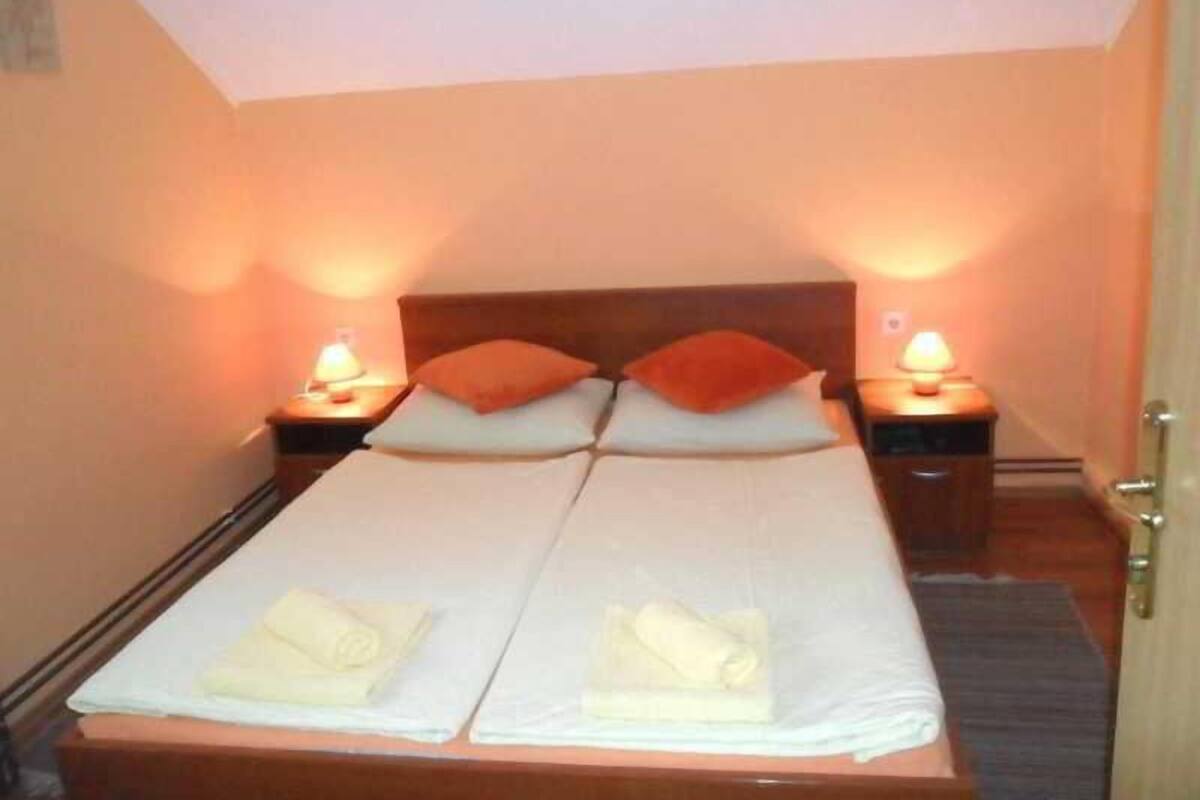A double bed with two pillows, a nightstand with a lamp, and a door to the right.