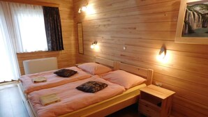 Ein schlicht eingerichtetes Schlafzimmer im Blockhausstil mit zwei Betten, einem Nachttisch und einer kleiner Kommode.