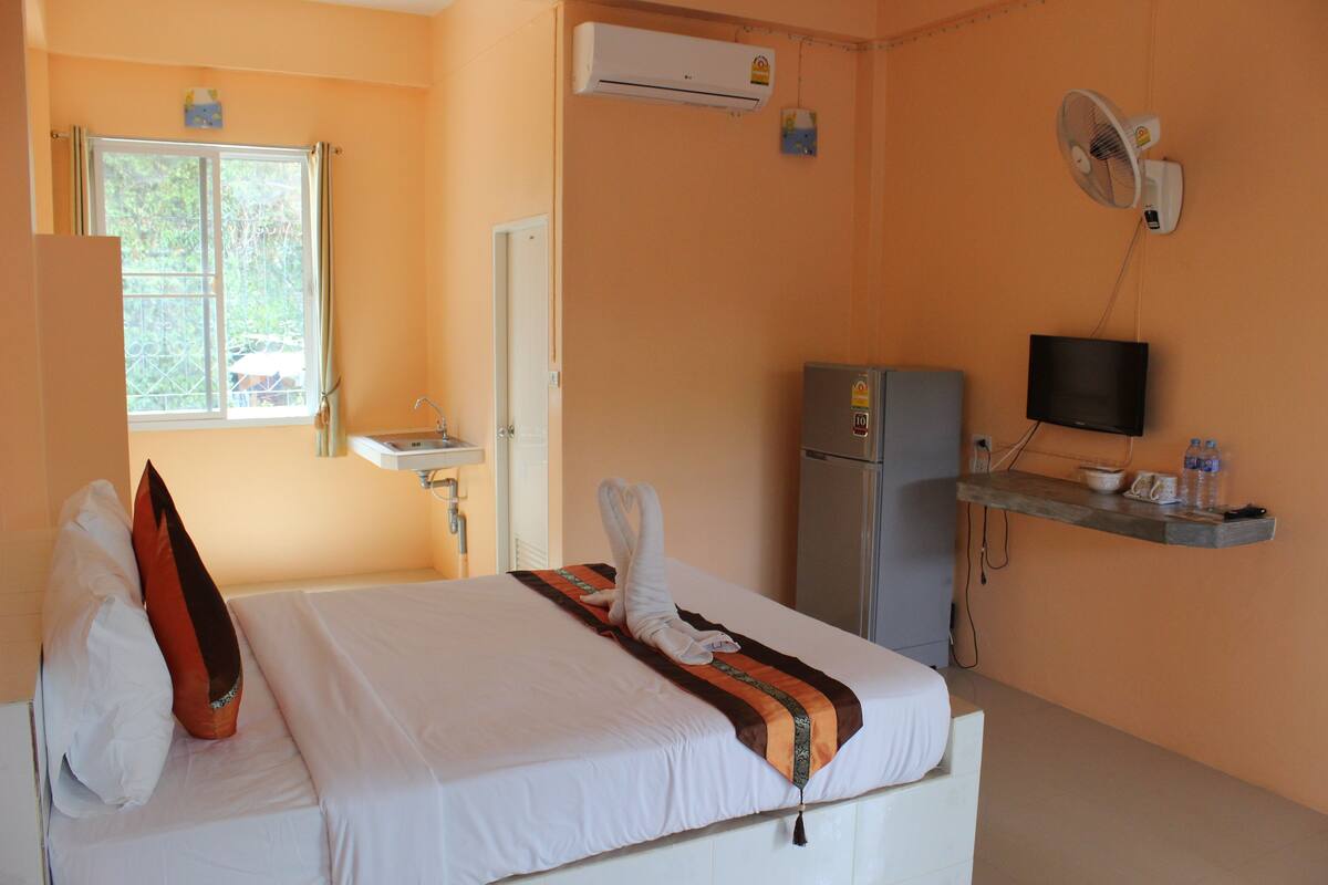 A hotel room with a bed, a TV, a refrigerator, and an air conditioning unit.