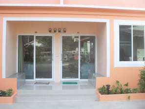 Entrada de un edificio con puerta de cristal, unos pocos escalones y un felpudo verde.