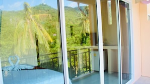 A room with a bed, a glass door leading to a balcony with a view of palm trees and a mountain. - Budchui Village 2 (Koh Tao)