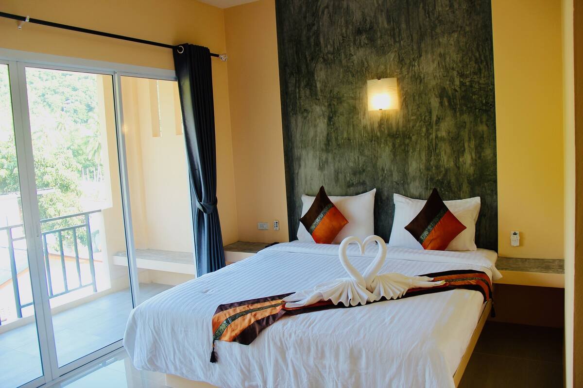 A hotel room with a large bed, a balcony with a view, and a wall-mounted light fixture.