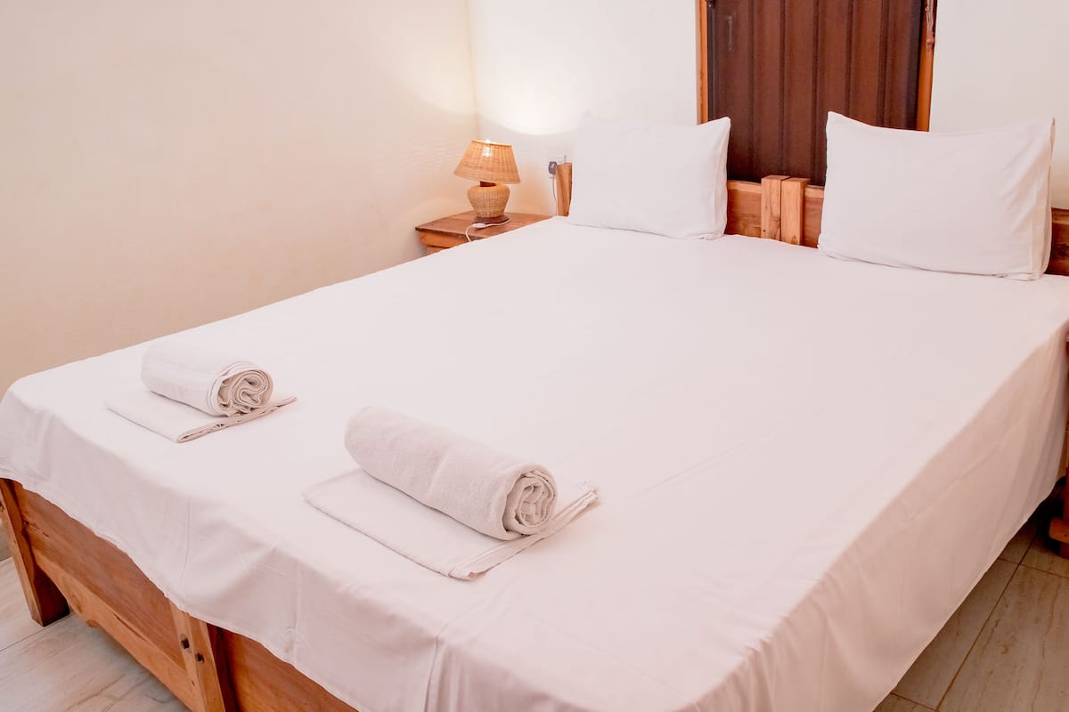 Cama bem arrumada com lençóis brancos e duas toalhas enroladas no painel da cabeceira.