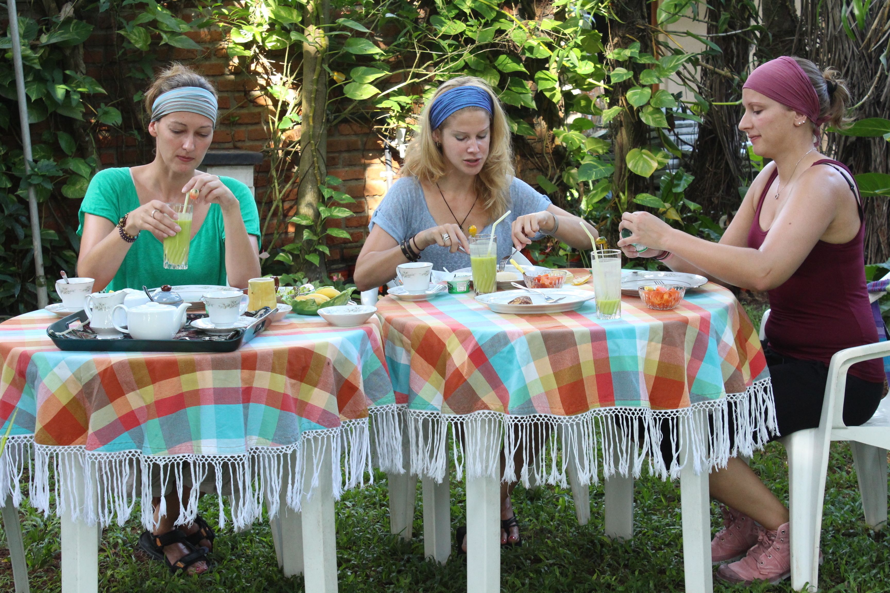 Three people dining at an outdoor table with a colorful tablecloth, surrounded by greenery.